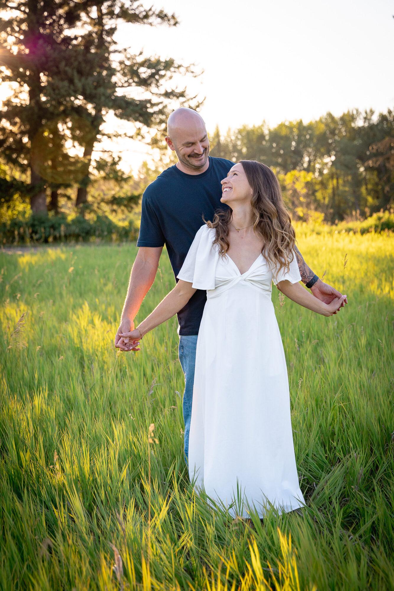Couple holding hands and smiling at each other in a grassy field with mountain backdrop