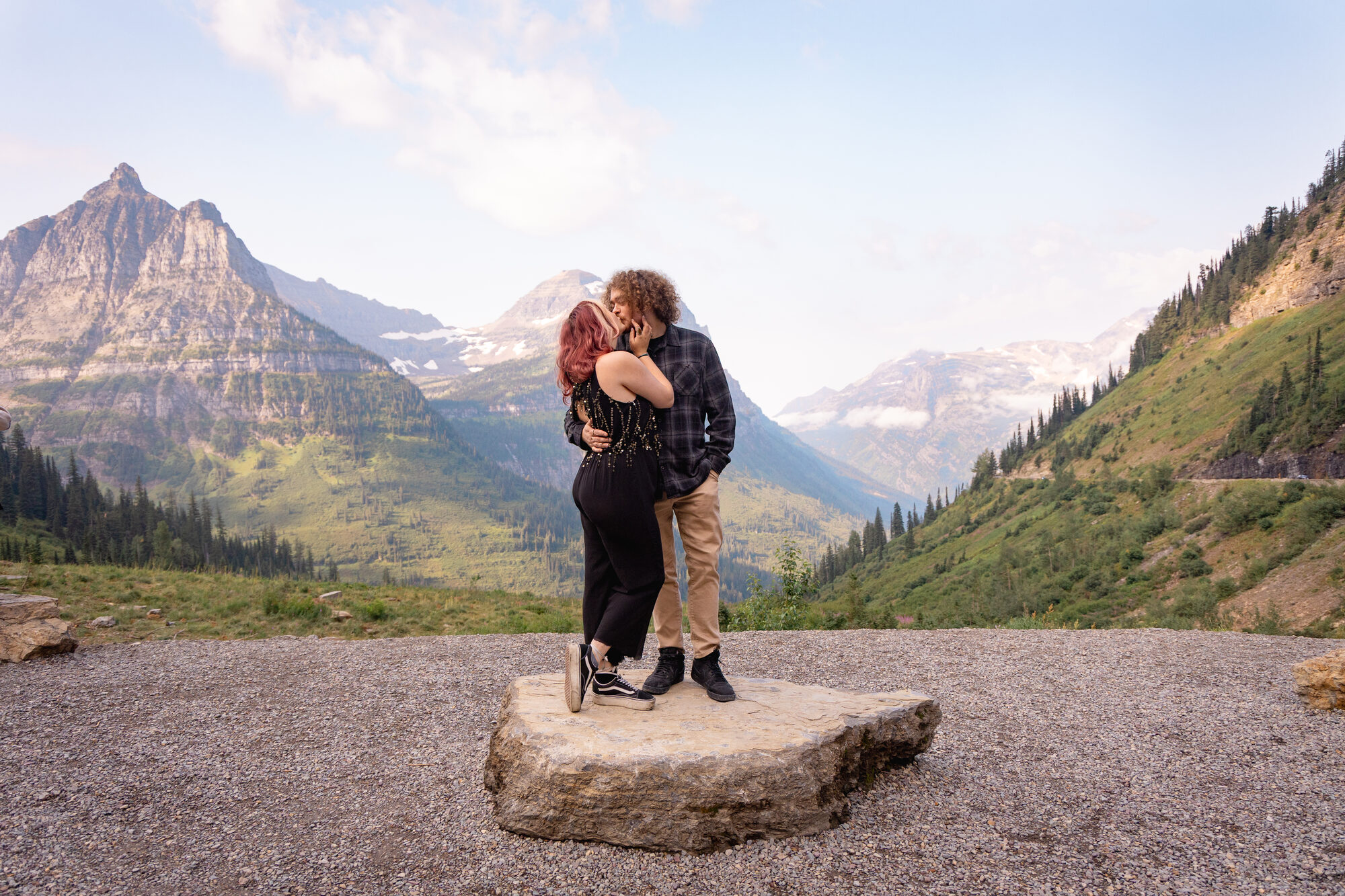 Couple kissing on a granite overlook with layered mountain peaks behind them